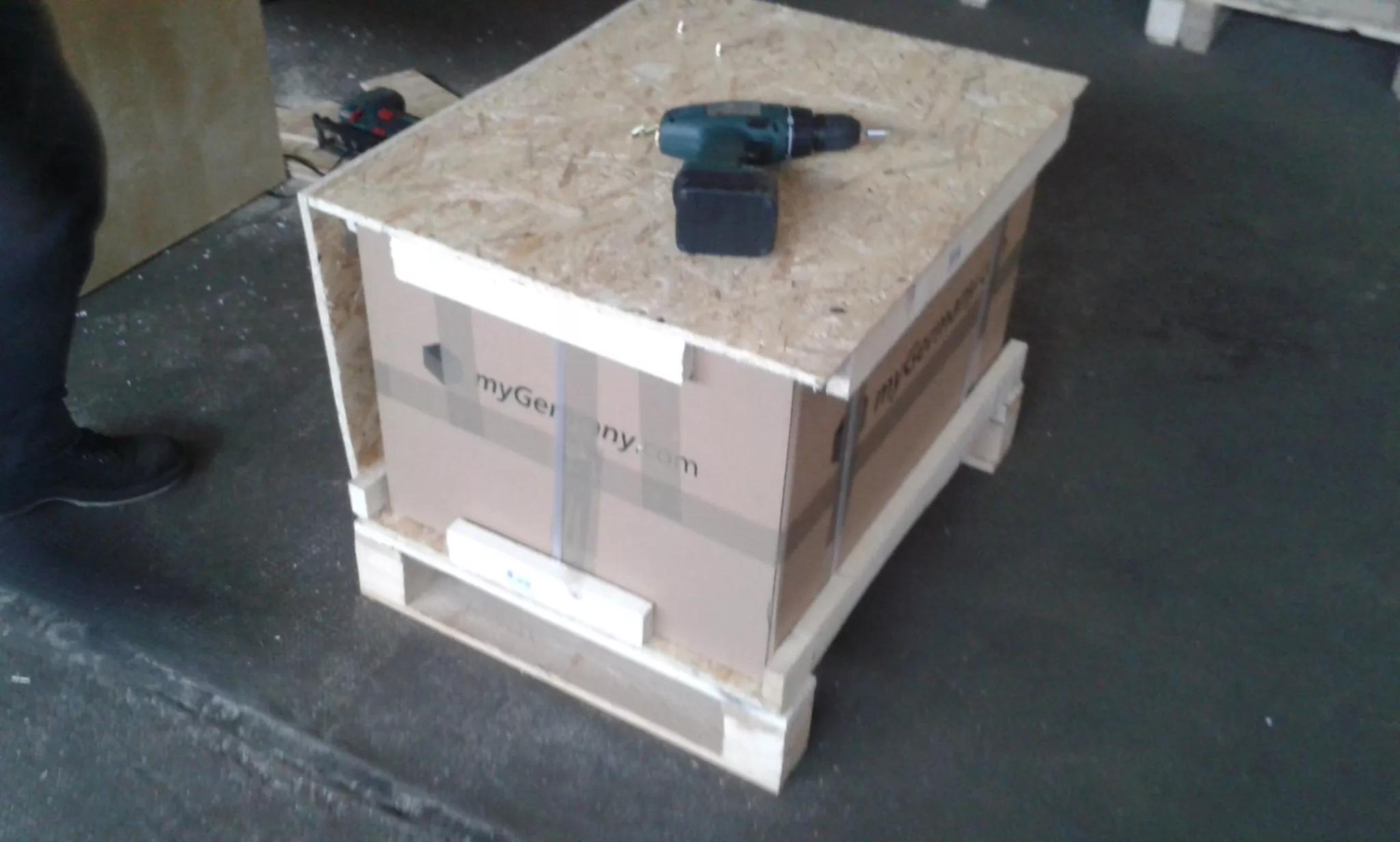 Holzkiste mit verpacktem Karton, auf dem eine Bohrmaschine steht