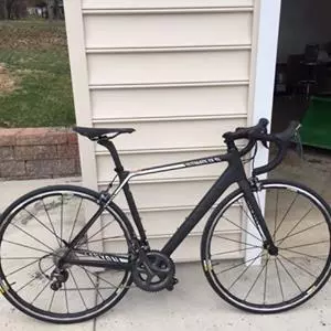 Ein schwarz-weißes Rennrad lehnt an einer beigen Garagenwand.